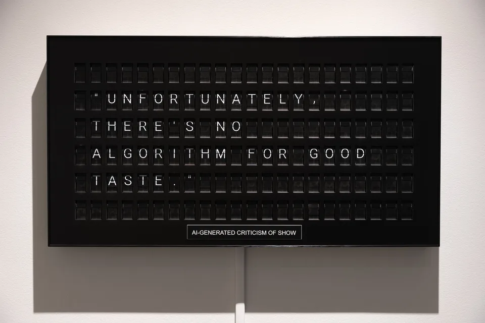The split-flap board displays a generated criticism about an algorithm for good taste.