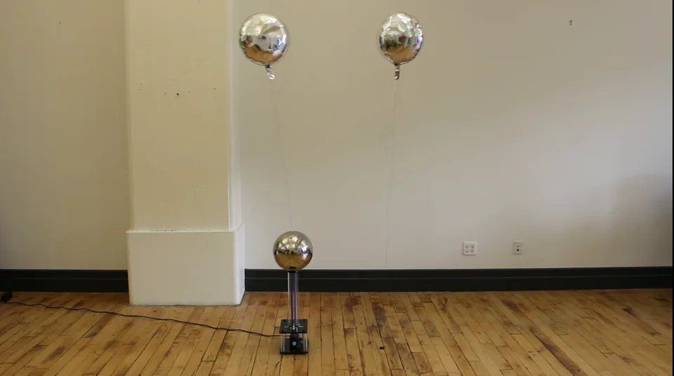 Two silver Mylar balloons suspended near one another above an electrostatic generator