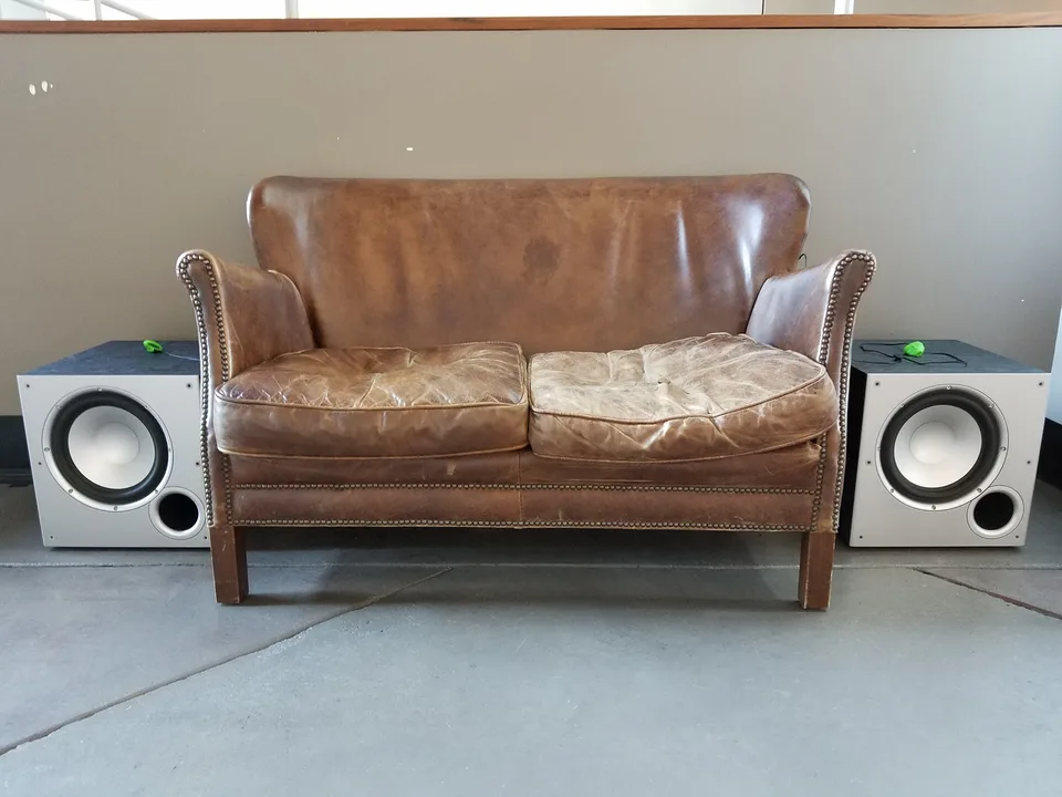 A worn leather loveseat flanked by two speakers in paired pulse annunciator