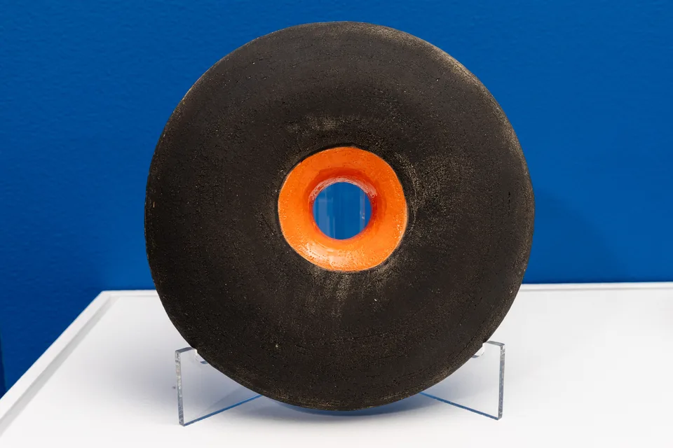 A black ceramic ring with an orange inner opening on a clear stand against a blue wall.