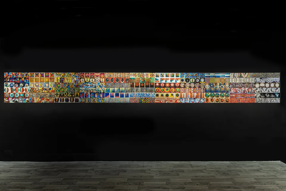Rows of small colorful images stretch across a long horizontal strip on a black wall.