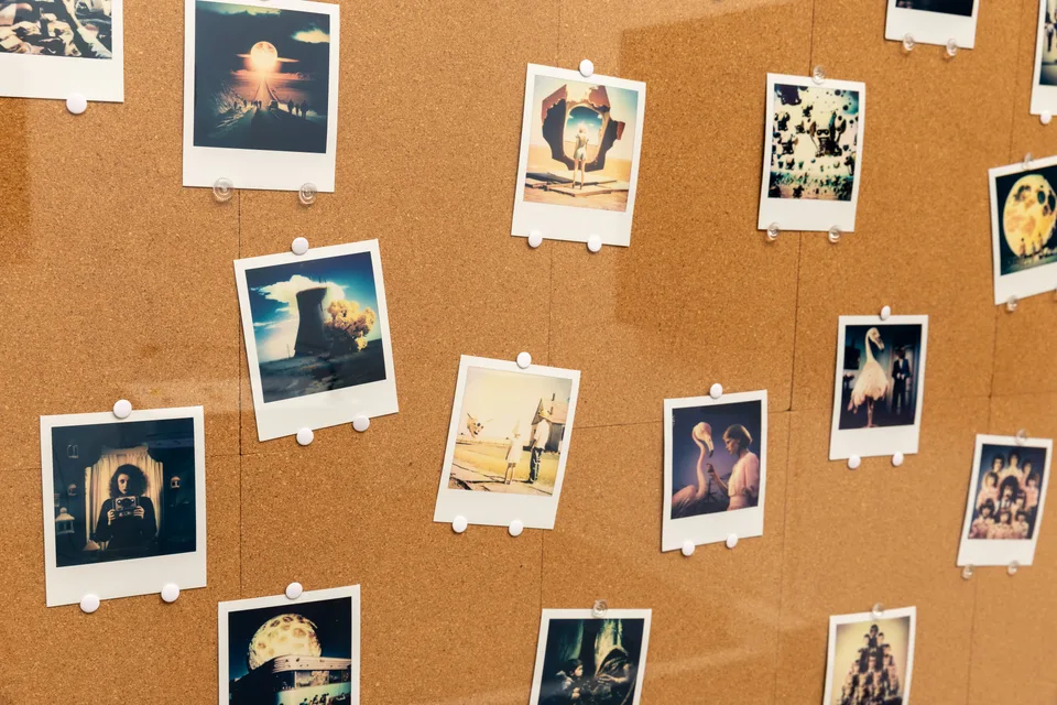 A detail of small instant photographs pinned to the cork board.