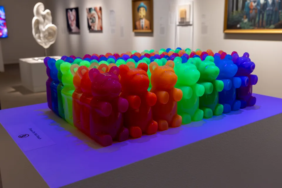 Rows of translucent red, green, blue, orange, and purple bear-like resin figures fill a white plinth.