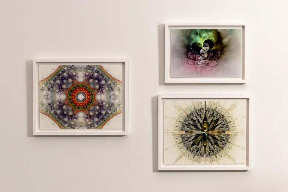 Three framed generative prints: a multicolored circular pattern at left, looping green and purple forms at upper right, and a radial black and gold composition at lower right.