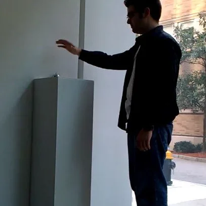 A visitor reaching toward a small desk bell on a tall white pedestal
