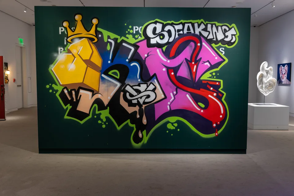 Large yellow, pink, red, and blue graffiti forms fill a green freestanding gallery wall.