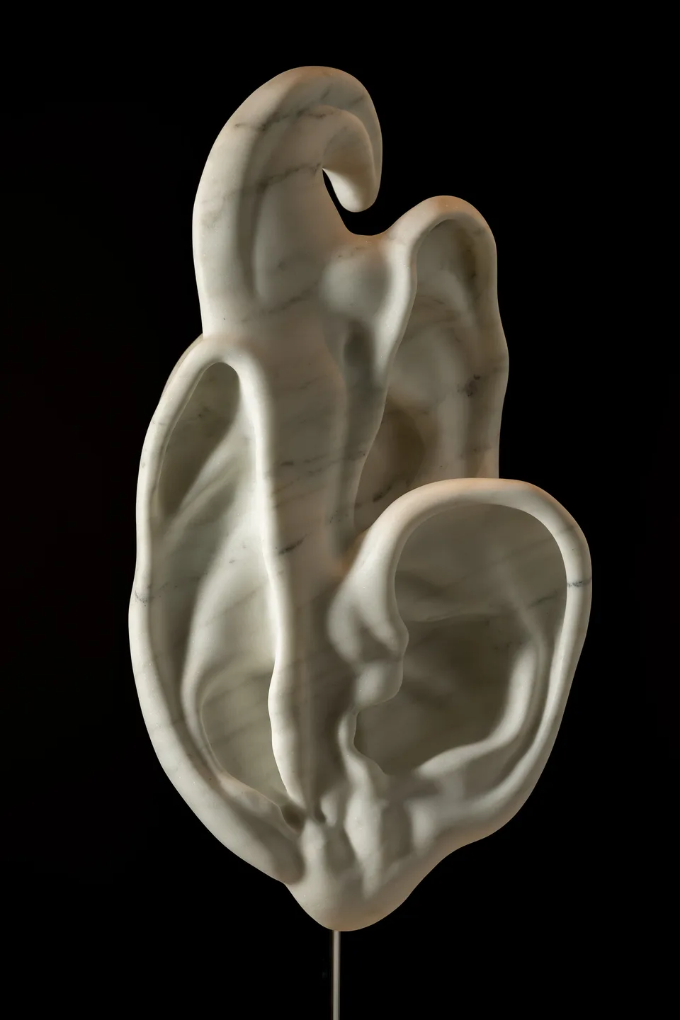 An ear-like white marble sculpture photographed against a dark background.