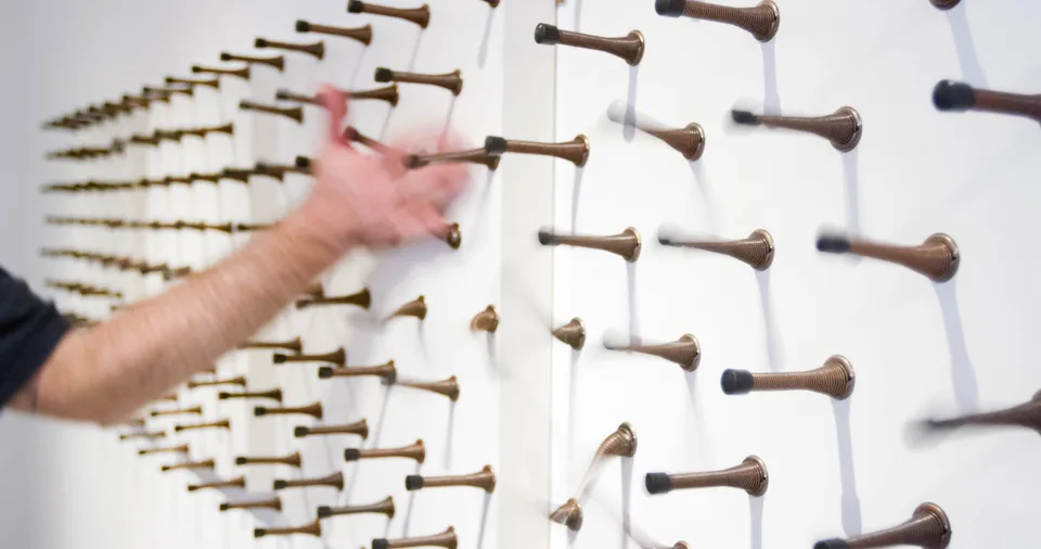 A hand reaching toward rows of spring door stops mounted on white panels