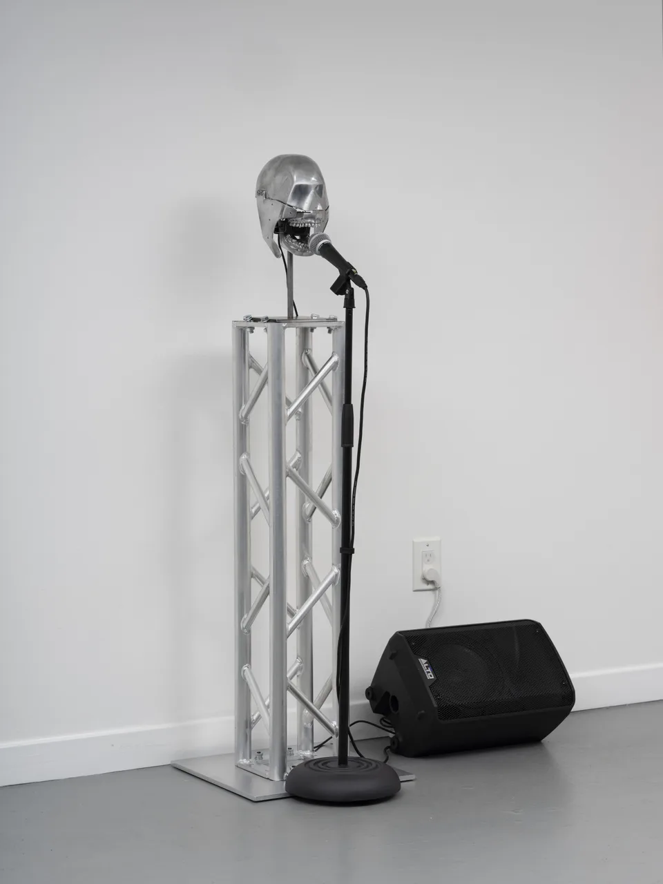 A metal dental phantom stands on an aluminum truss beside a microphone and a black amplified speaker.