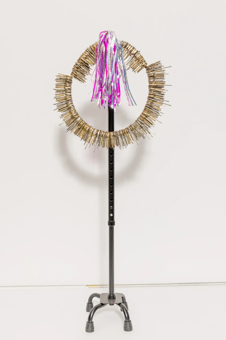 A black four-footed cane supports a circular arrangement of keys and metallic ribbons.