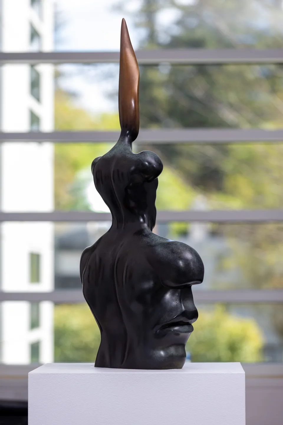 Rear three-quarter view of the bronze bust beside a window.