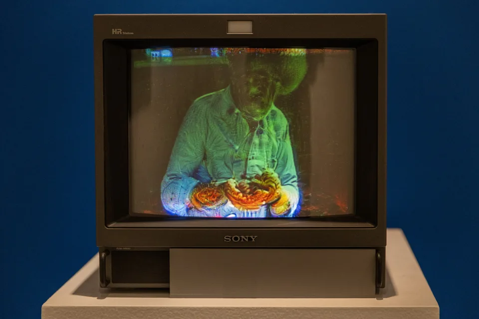 A CRT monitor showing a distorted colorful image of a seated painter.