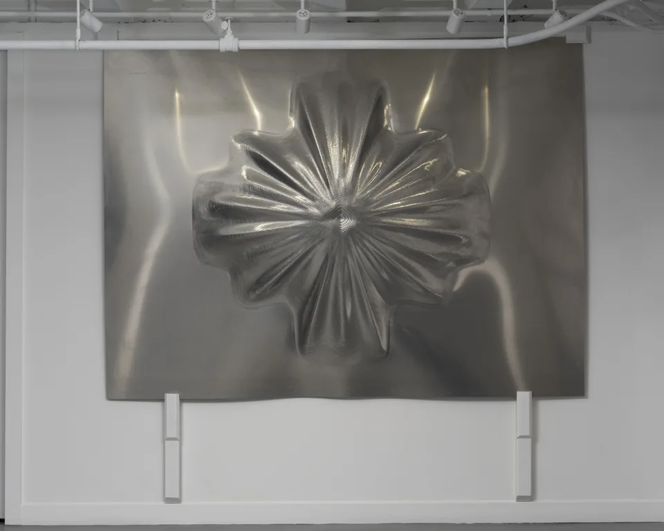 A large rectangular aluminum panel bulges into a radial flower-like relief, with densely rippled metal surfaces.