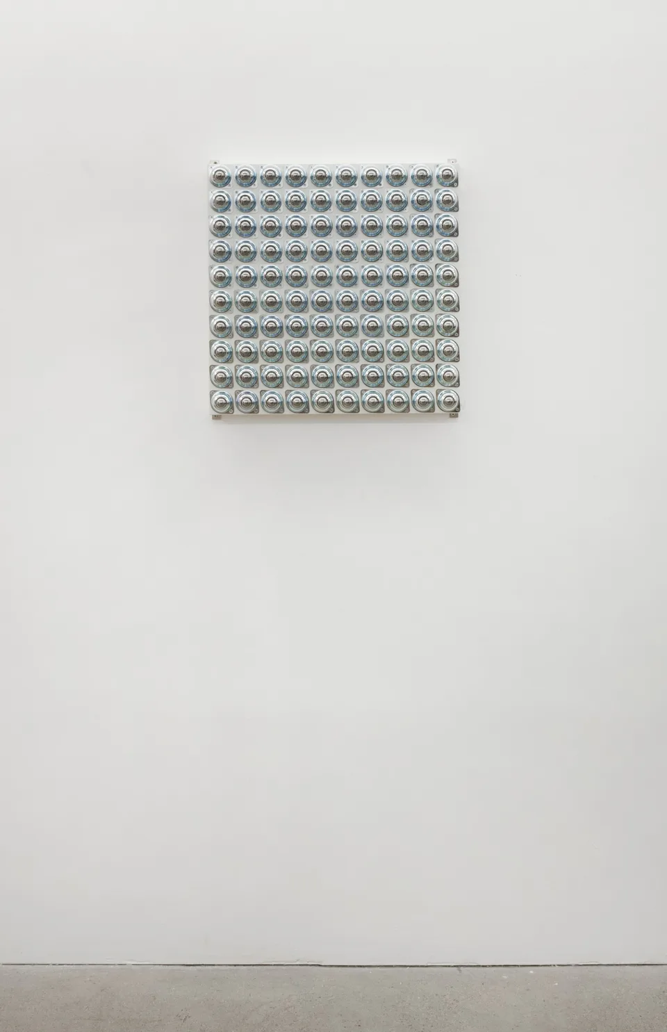 A grid of circular metal fittings shown on the gallery wall