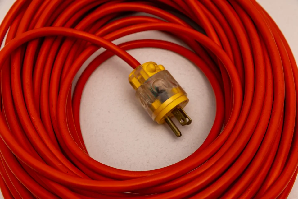 A close-up of a coiled orange extension cord and its transparent yellow-ended electrical plug.