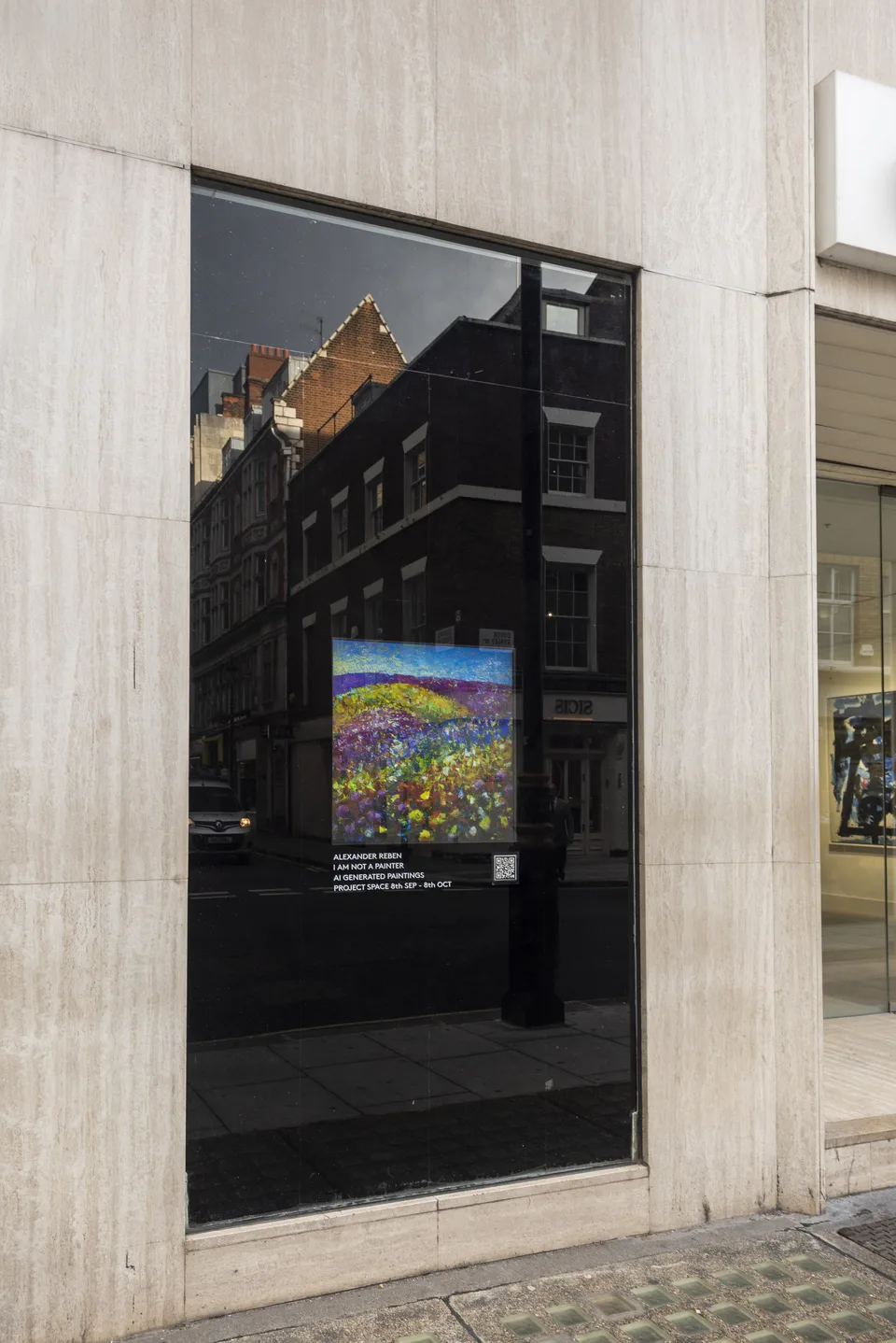 A colorful landscape appears on a screen in the gallery window above the exhibition announcement, with buildings reflected in the glass.