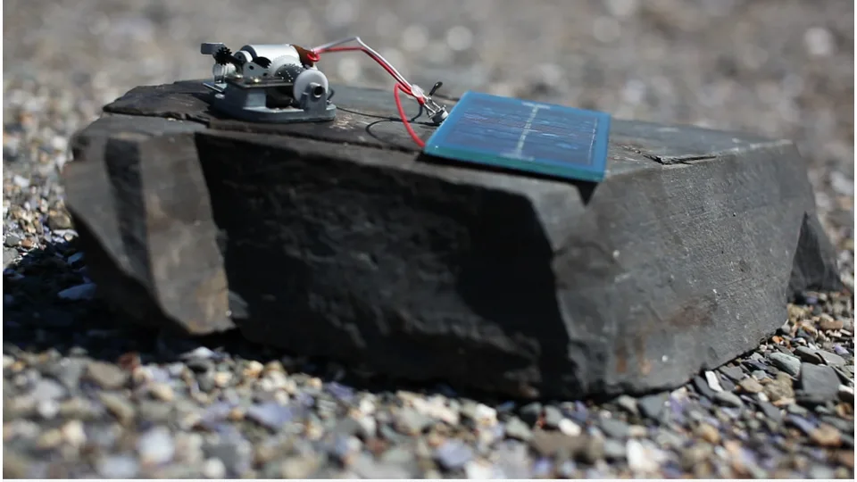 A solar panel and music-box mechanism placed on a rock outdoors