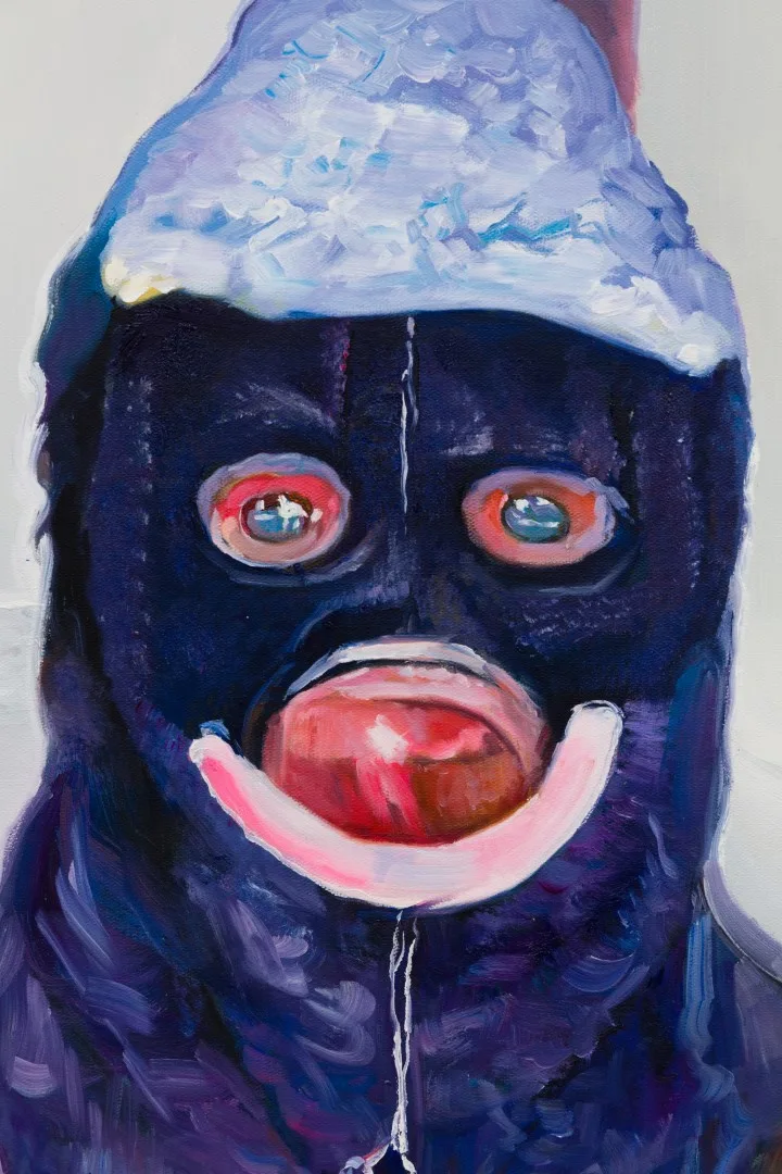 Detail of a dark blue painted head with bright outlined eyes, pink lips and a pale cap.