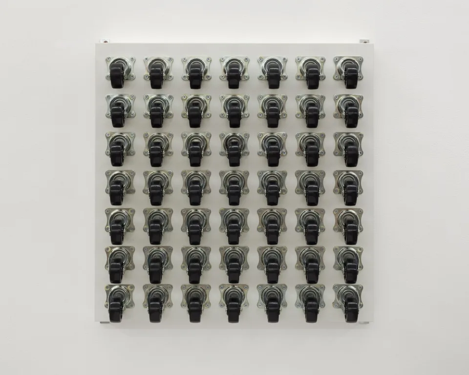 Black caster wheels arranged in a regular grid on a white square panel