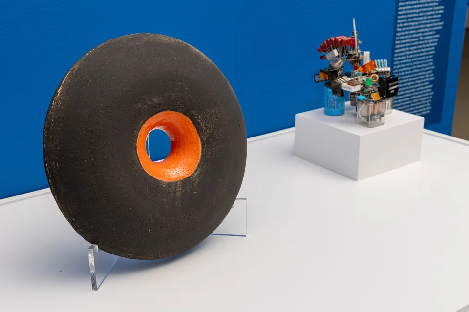 The black and orange ceramic ring in the foreground, with the electronic-component assemblage further along the plinth.