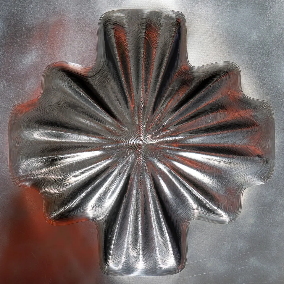 Close view of the cross-shaped aluminum relief with radial ridges on the forming machine, reflecting an orange robot.