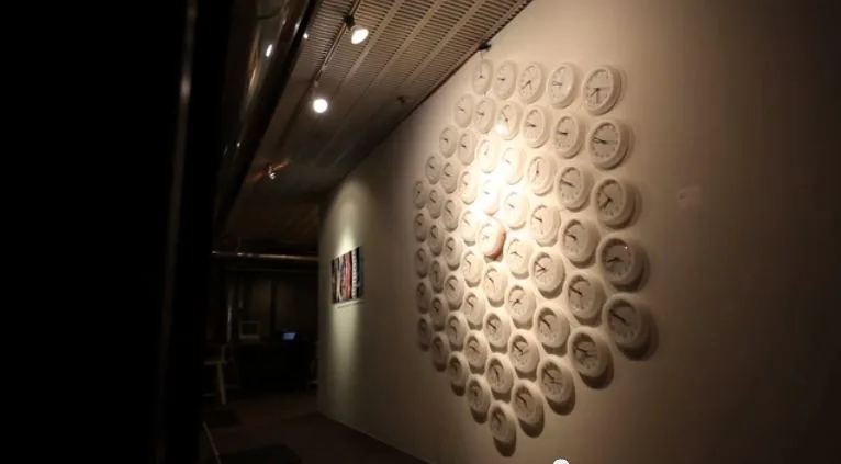 Sixty white wall clocks arranged together on a gallery wall