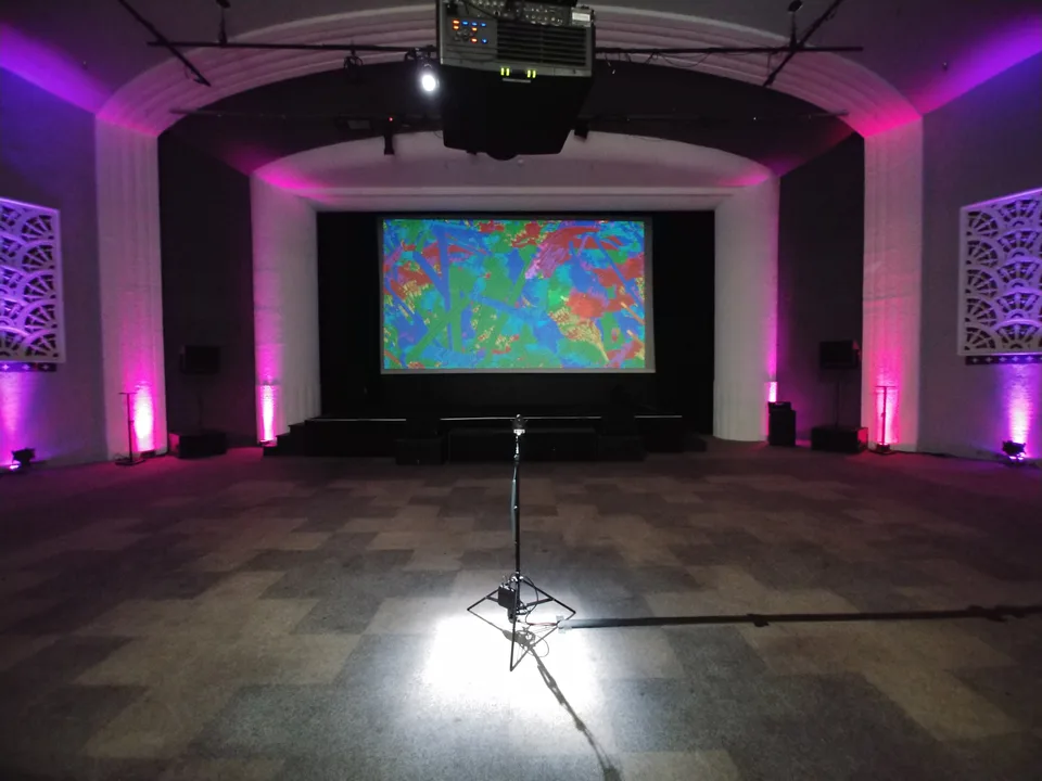 A TokenArt installation with a microphone facing a large projection in a purple-lit room
