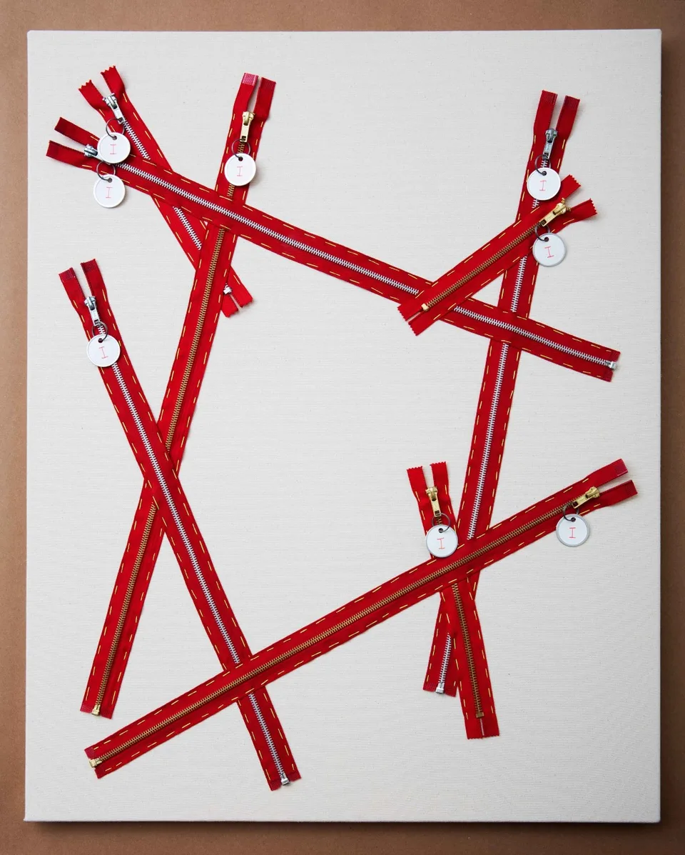 Red zippers crisscross a white canvas, with round white tags bearing a red I attached to their pulls.