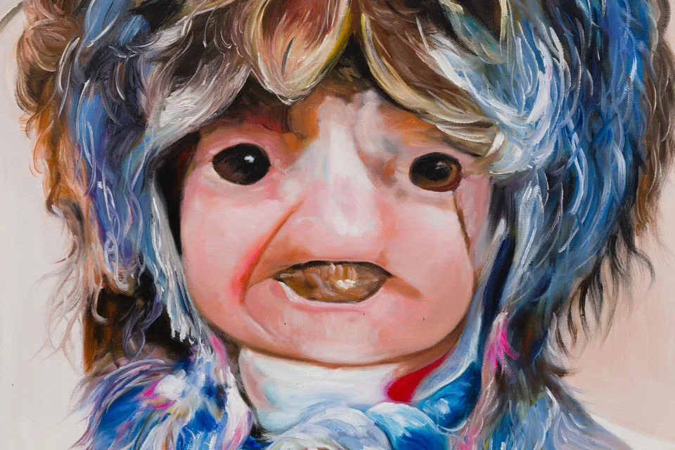 Detail of a doll-like painted face with dark eyes and layers of blue and brown hair.