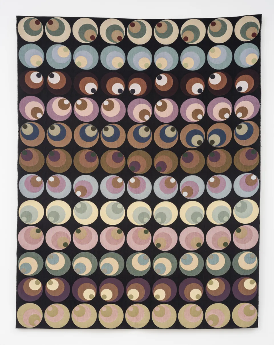 Rows of nested pastel circles form an eye-like pattern on a black tapestry.