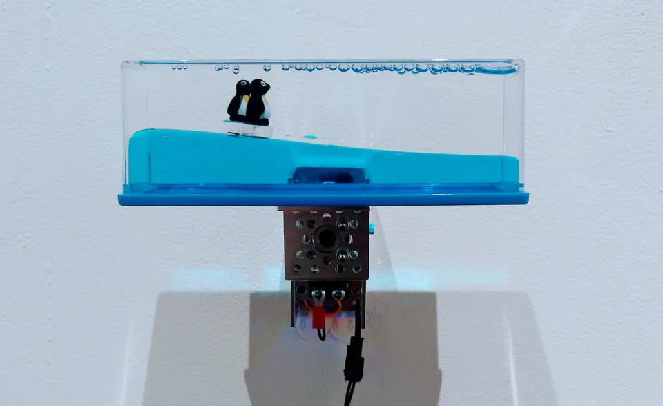 A small motor turns a blue liquid-filled novelty toy with floating penguins in Toybots