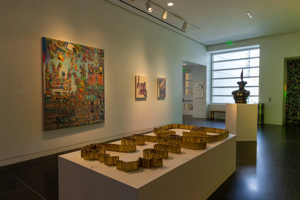 A winding arrangement of brass hinges fills a long plinth, with a large detailed painting and a bronze bust near the window.