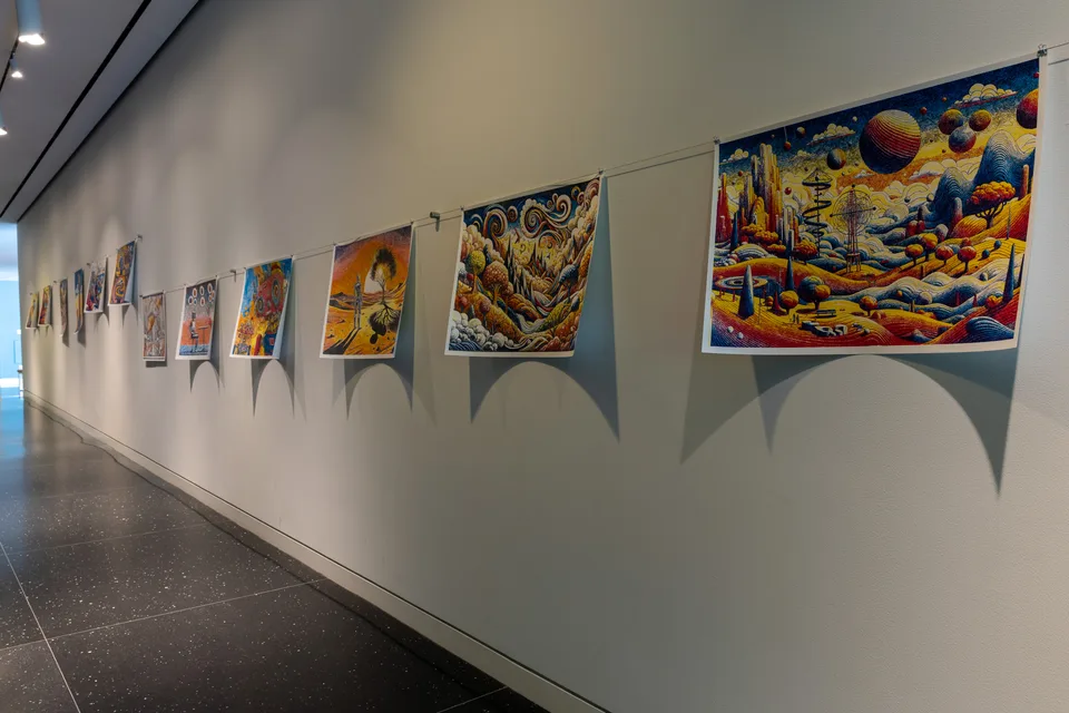 A line of colorful prints hangs from wires along a long white corridor wall.