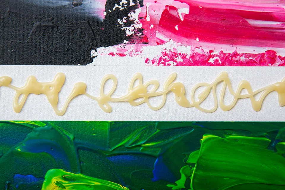 Close view of raised pale glue loops on a white band between thick pink, black and green paint.