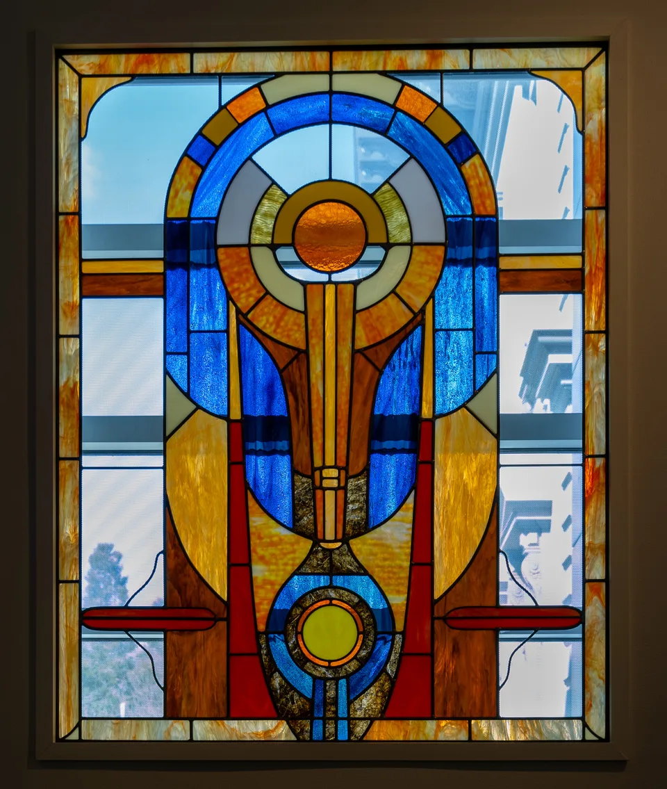 A stained-glass panel combines blue arcs, amber circles, red accents, and a symmetrical central vertical form.