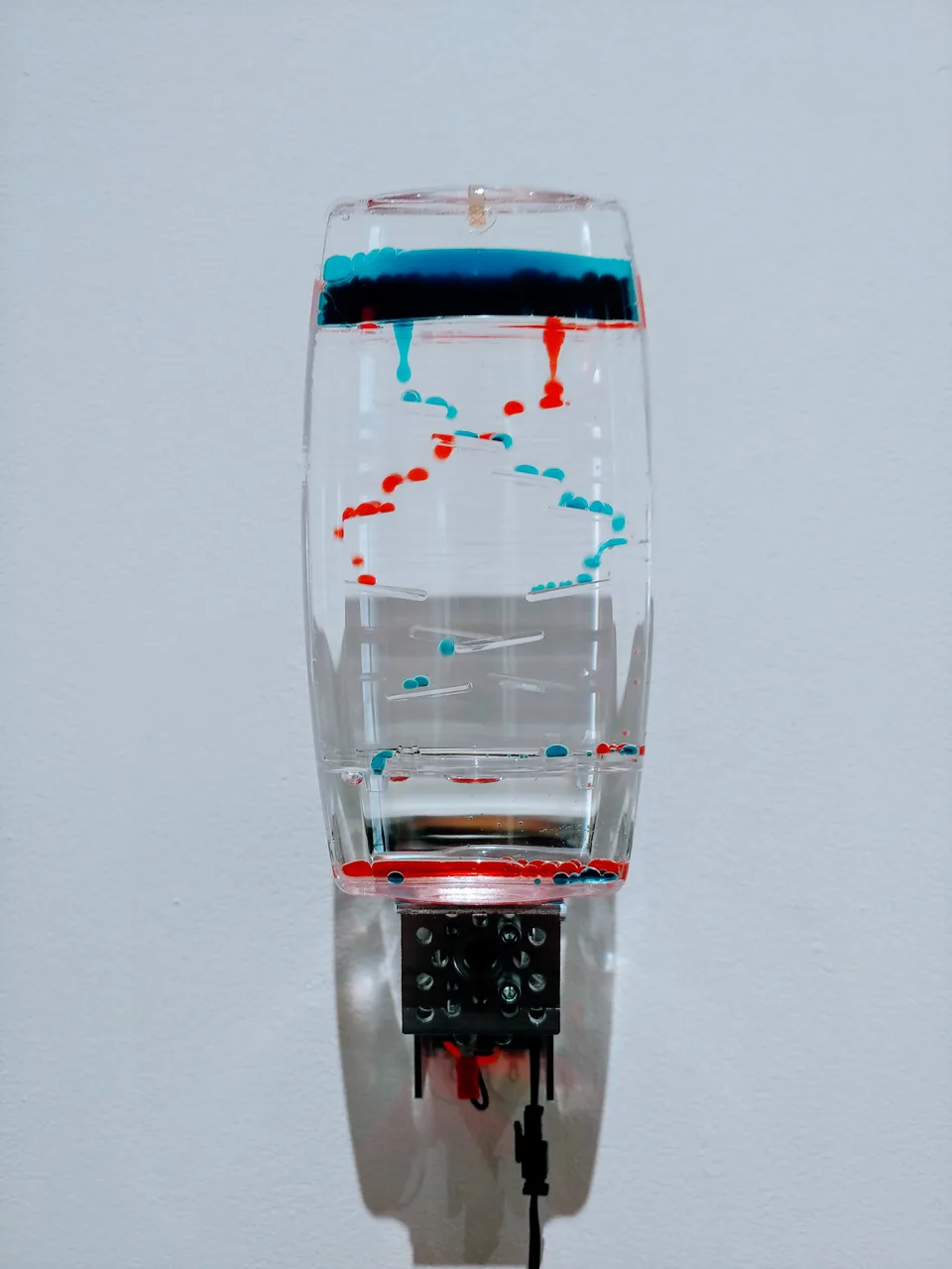 A transparent toy containing red and blue liquid droplets is attached to an exposed motorized mechanism.