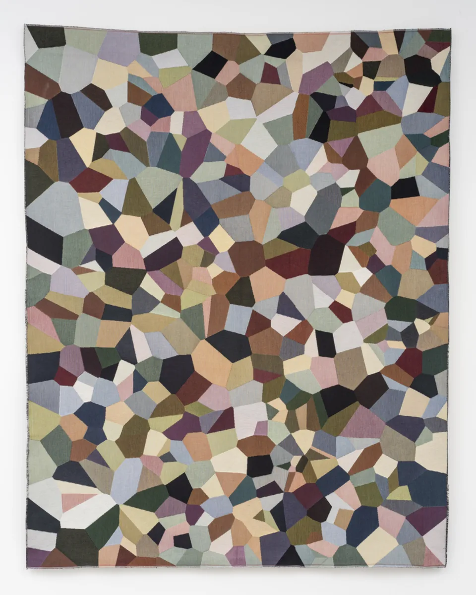 Irregular polygons in muted pink, blue, green, yellow, and brown cover a rectangular tapestry.