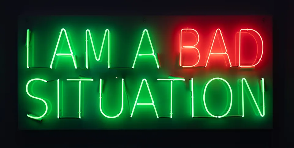 Green and red neon lettering reads I AM A BAD SITUATION against a dark background.